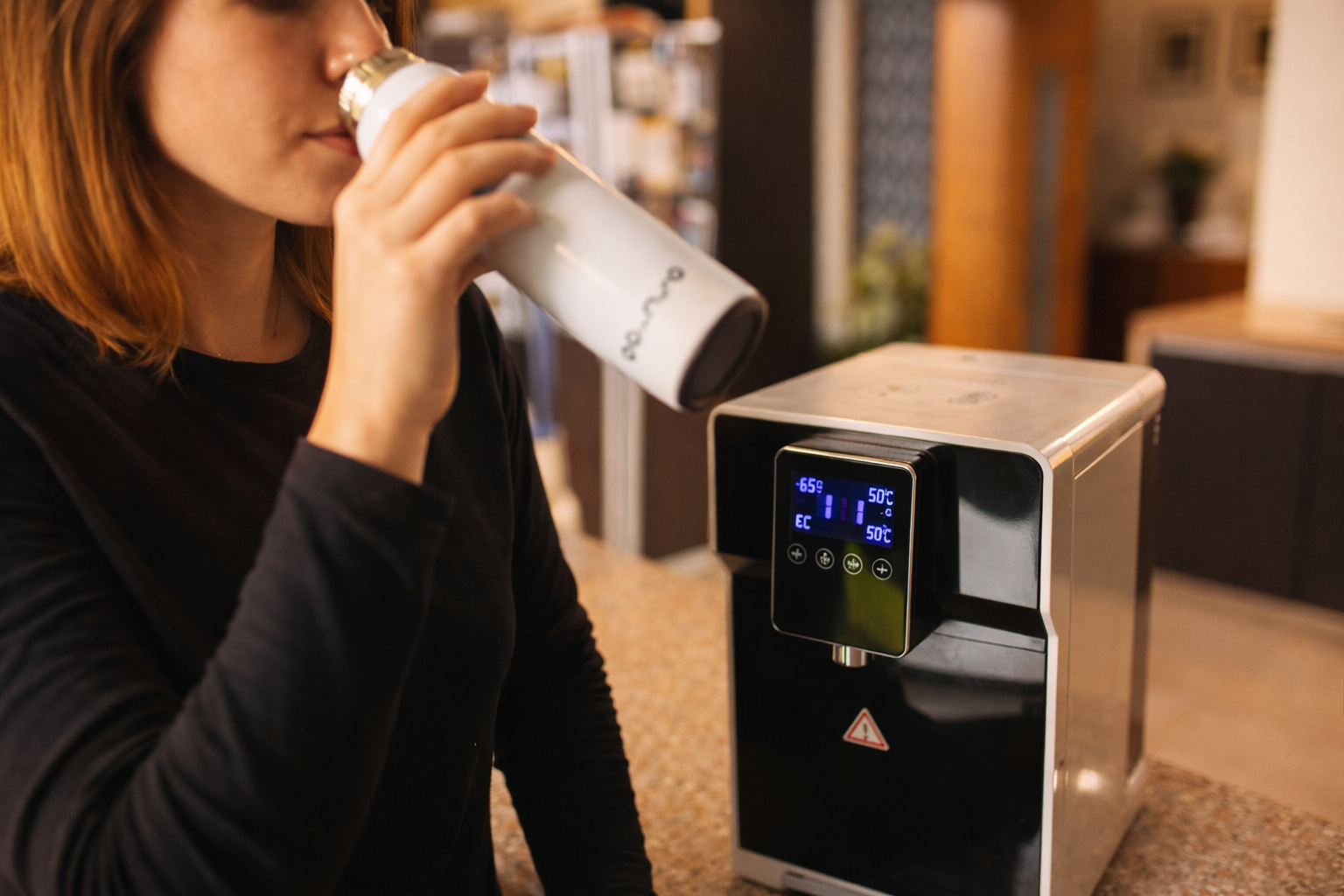Persona tomando agua purificada junto a un purificador de ósmosis inversa en casa.
